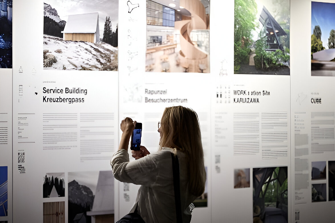 eine frau betrachtet eine ausstellung von architect@work düsseldorf 2023 bildern an einer wand.