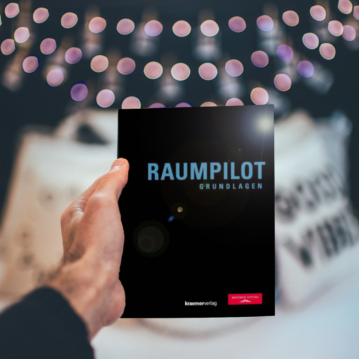 Eine Person hält ein Buch mit dem Wort „Raumplot“ hoch, das bei der Wüstenrot Stiftung zum kostenlosen Download erhältlich ist.