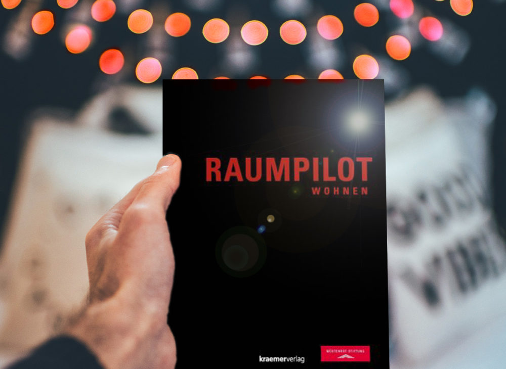 Eine Person hält ein kostenlos herunterladbares Buch „Raumpilot“ über Wohnen hoch.