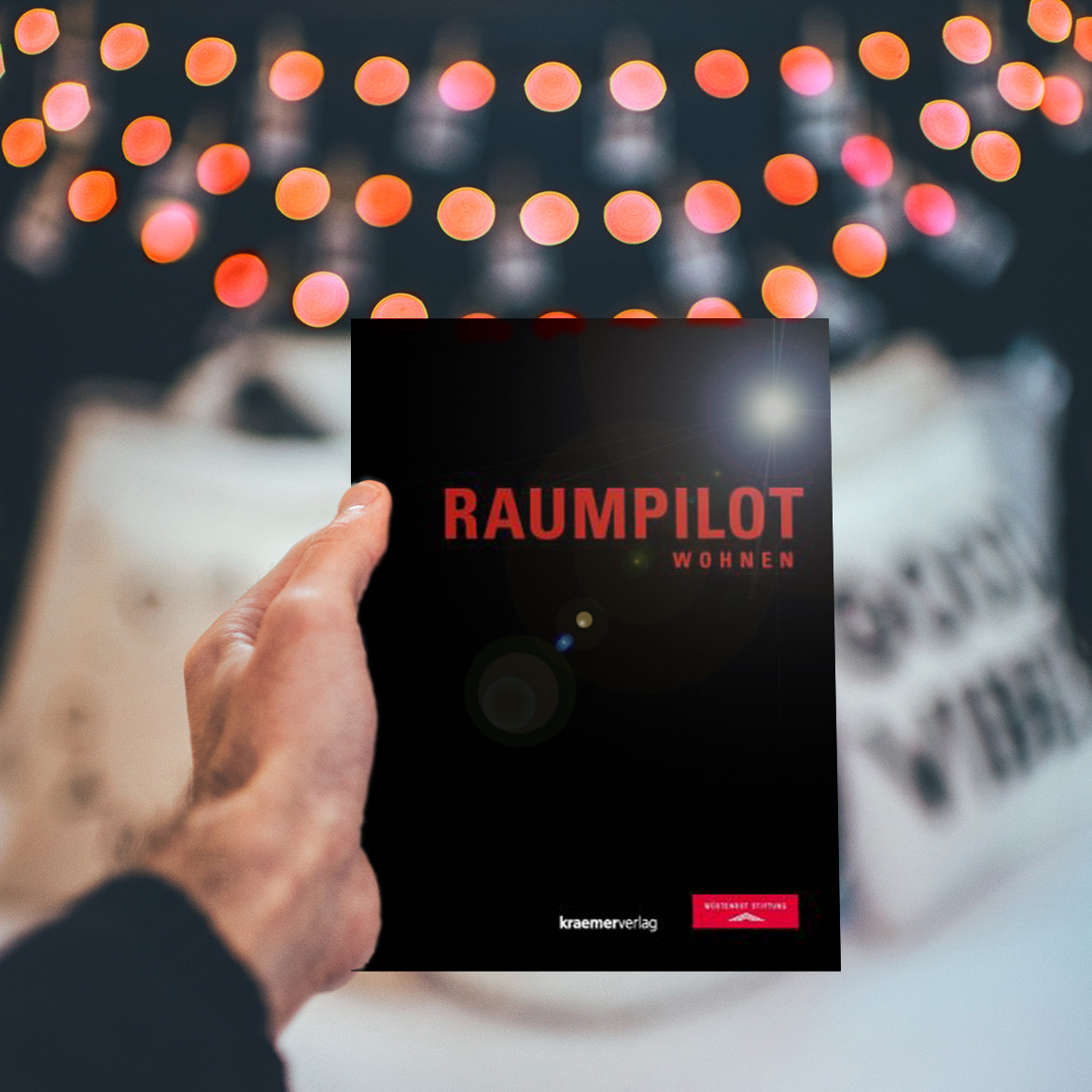 Eine Person hält ein kostenlos herunterladbares Buch „Raumpilot“ über Wohnen hoch.