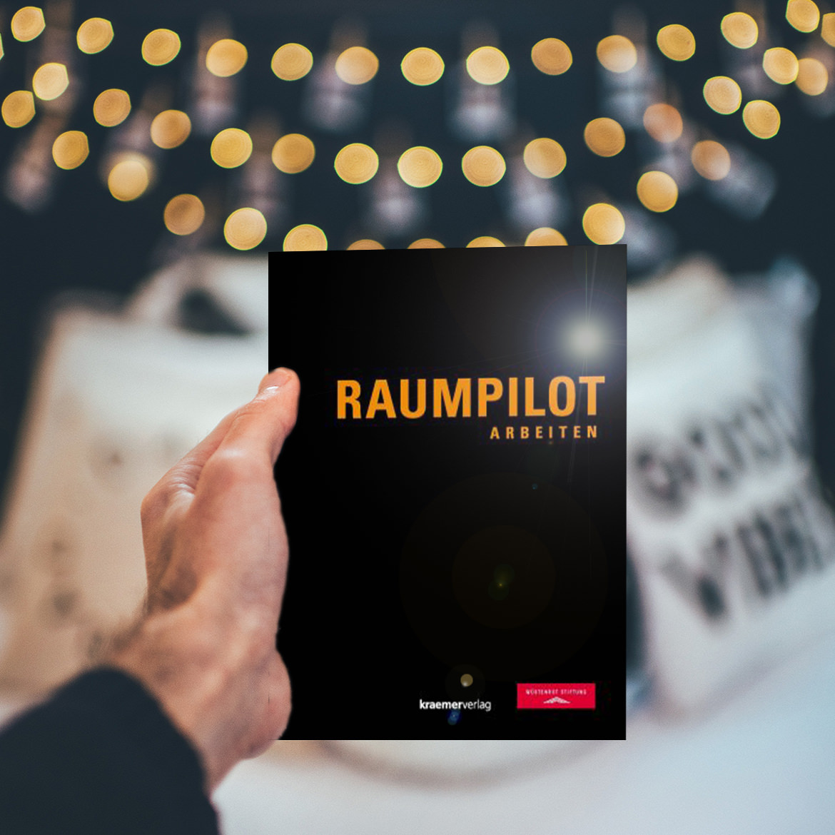 Eine Person hält ein Buch mit dem Titel „Raumplot“ hoch, das zum kostenlosen Download verfügbar ist.