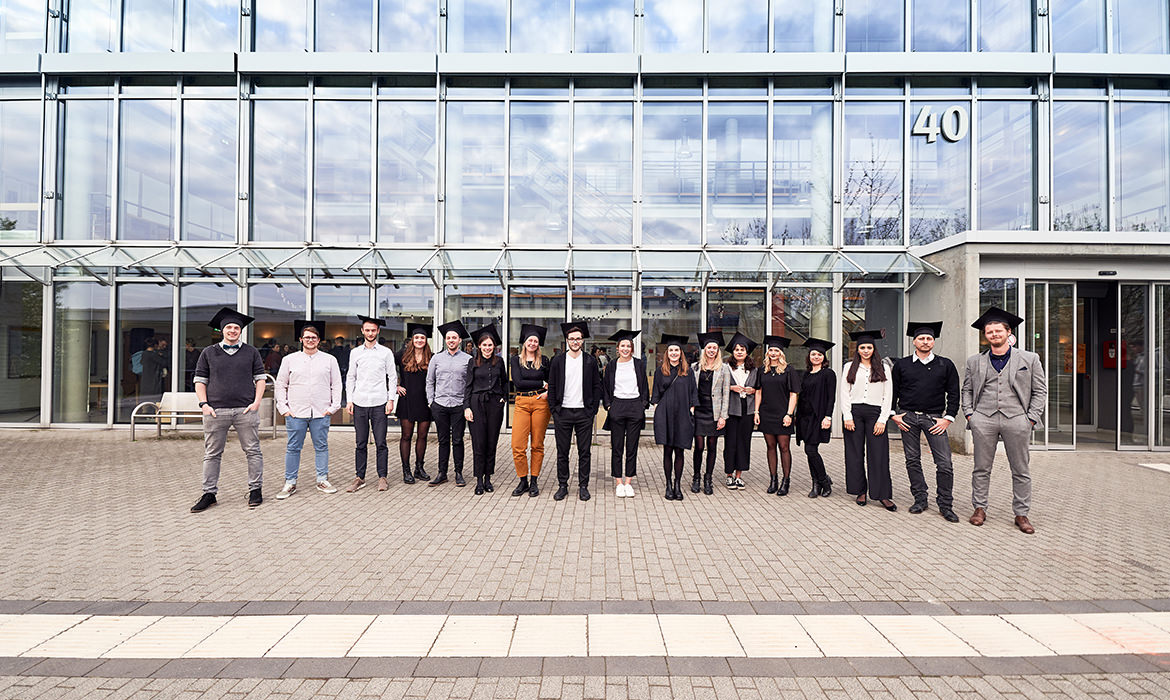 Eine Gruppe Bachelorabsolventen der FH Dortmund posiert vor einem Glasgebäude.