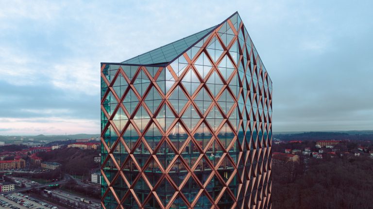 Modernes Bürogebäude aus Glas mit einer markanten Fassade im Rautenmuster, das die BIM-Methodik vor dem Hintergrund einer Stadtlandschaft unter bewölktem Himmel zur Geltung bringt. Erstellt mit Archciad 29. Kineum - Schweden Reflex Arkitekter reflexark.se